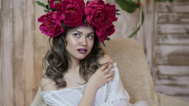 Kız model poz. başında kırmızı peonies çelenk genç bir kadın, siyah uzun kıvırcık saçlı küçük omuzlarında iner.