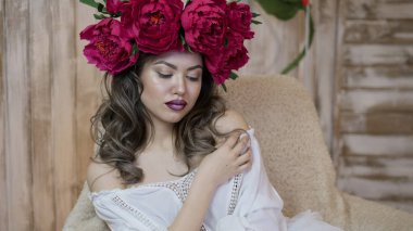 Kız model poz. başında kırmızı peonies çelenk genç bir kadın, siyah uzun kıvırcık saçlı küçük omuzlarında iner.