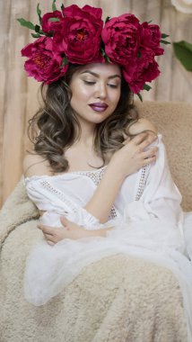 Kız model poz. başında kırmızı peonies çelenk genç bir kadın, siyah uzun kıvırcık saçlı küçük omuzlarında iner.