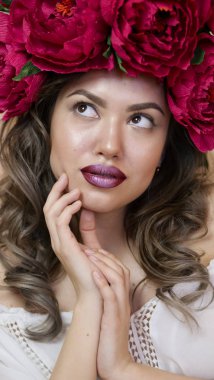 Kız model poz. başında kırmızı peonies çelenk genç bir kadın, siyah uzun kıvırcık saçlı küçük omuzlarında iner.