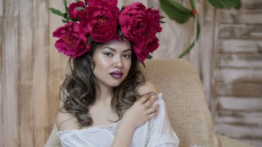 Kız model poz. başında kırmızı peonies çelenk genç bir kadın, siyah uzun kıvırcık saçlı küçük omuzlarında iner.