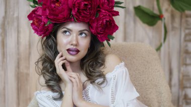 Kız model poz. başında kırmızı peonies çelenk genç bir kadın, siyah uzun kıvırcık saçlı küçük omuzlarında iner.