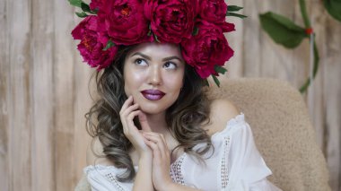 Kız model poz. başında kırmızı peonies çelenk genç bir kadın, siyah uzun kıvırcık saçlı küçük omuzlarında iner.