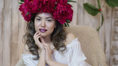 Kız model poz. başında kırmızı peonies çelenk genç bir kadın, siyah uzun kıvırcık saçlı küçük omuzlarında iner.