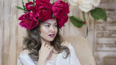 Kız model poz. başında kırmızı peonies çelenk genç bir kadın, siyah uzun kıvırcık saçlı küçük omuzlarında iner.