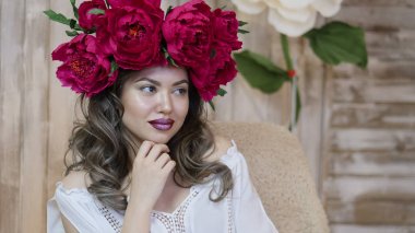 Kız model poz. başında kırmızı peonies çelenk genç bir kadın, siyah uzun kıvırcık saçlı küçük omuzlarında iner.