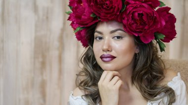 Kız model poz. başında kırmızı peonies çelenk genç bir kadın, siyah uzun kıvırcık saçlı küçük omuzlarında iner.