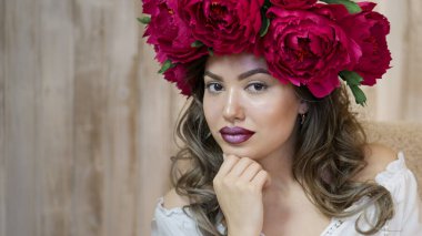 Kız model poz. başında kırmızı peonies çelenk genç bir kadın, siyah uzun kıvırcık saçlı küçük omuzlarında iner.