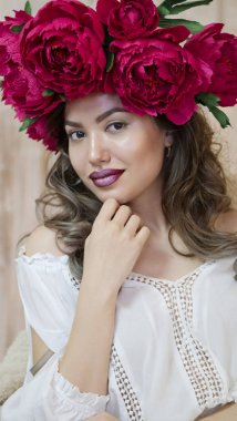 Kız model poz. başında kırmızı peonies çelenk genç bir kadın, siyah uzun kıvırcık saçlı küçük omuzlarında iner.