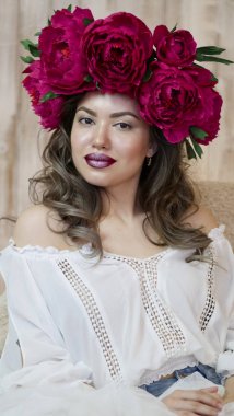 Kız model poz. başında kırmızı peonies çelenk genç bir kadın, siyah uzun kıvırcık saçlı küçük omuzlarında iner.
