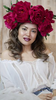 Kız model poz. başında kırmızı peonies çelenk genç bir kadın, siyah uzun kıvırcık saçlı küçük omuzlarında iner.