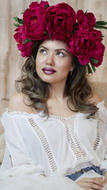 Kız model poz. başında kırmızı peonies çelenk genç bir kadın, siyah uzun kıvırcık saçlı küçük omuzlarında iner.