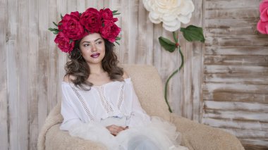 Kız model poz. başında kırmızı peonies çelenk genç bir kadın, siyah uzun kıvırcık saçlı küçük omuzlarında iner.