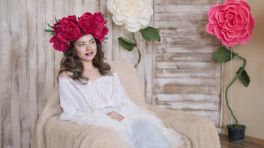 Kız model poz. başında kırmızı peonies çelenk genç bir kadın, siyah uzun kıvırcık saçlı küçük omuzlarında iner.