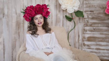 Kız model poz. başında kırmızı peonies çelenk genç bir kadın, siyah uzun kıvırcık saçlı küçük omuzlarında iner.