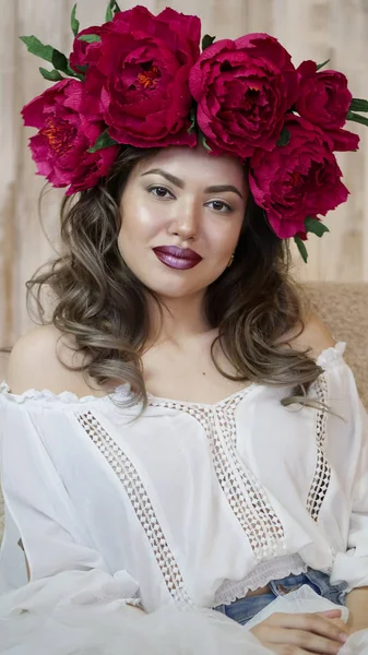 Kız model poz. başında kırmızı peonies çelenk genç bir kadın, siyah uzun kıvırcık saçlı küçük omuzlarında iner.