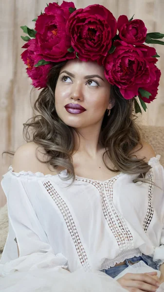 Kız model poz. başında kırmızı peonies çelenk genç bir kadın, siyah uzun kıvırcık saçlı küçük omuzlarında iner.