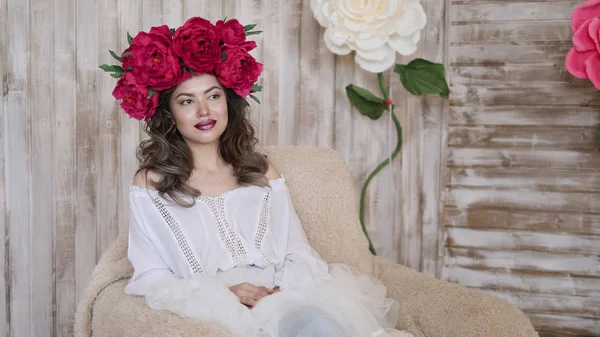 Kız model poz. başında kırmızı peonies çelenk genç bir kadın, siyah uzun kıvırcık saçlı küçük omuzlarında iner.