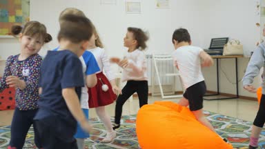 Çocuk Oyun Odası geliştirmek. Sınıflar eğlenceli sırasında duygular genç çocuk. Yastıklı turuncu tabureler ve üstüne düşmek çocuk bir parlak koşmak.