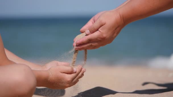 Pihenj a tengeren a gyerekekkel. A homokot a tenyeréből a gyermek tenyerébe öntik.. — Stock videók