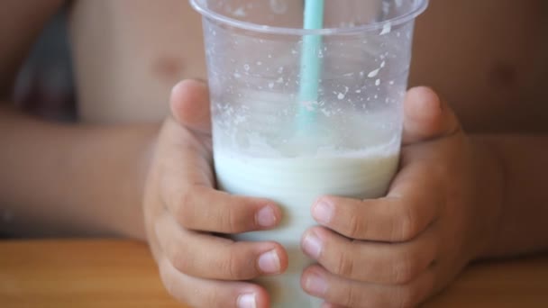 男の子はわらを通してミルクセーキを飲む 子供はチューブを通して吹き 泡を開始します 少年は両手で透明なガラスを持っている — ストック動画
