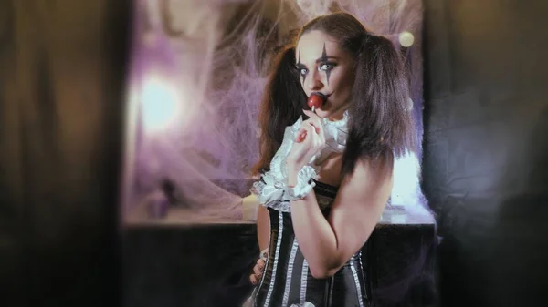 Portretul unei femei. Un clovn cu un zâmbet în corset cu un guler alb pe gât. Model cu machiaj de Halloween. Femeia flirtează. Fata cu acadea roşie . Imagine de stoc