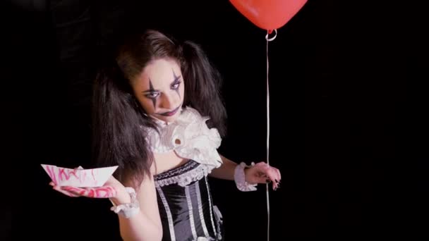 Easy Halloween Makeup. Girl with a red balloon, in the form of a clown. The woman holds out her hand with the white boat. On black background — Stock Video