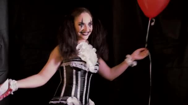 Легкий макіяж на Хеллоуїн. Дівчина з червоною кулею у формі клоуна. Жінка тримає руку з білим човном. На чорному тлі — стокове відео