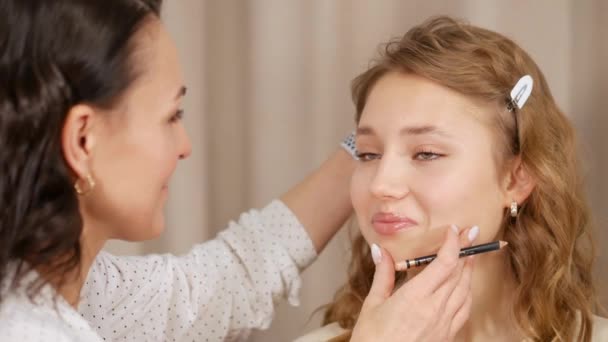Maquiagem mestre coloca maquiagem no rosto do cliente. Aplicando tinta nos lábios da menina . — Vídeo de Stock