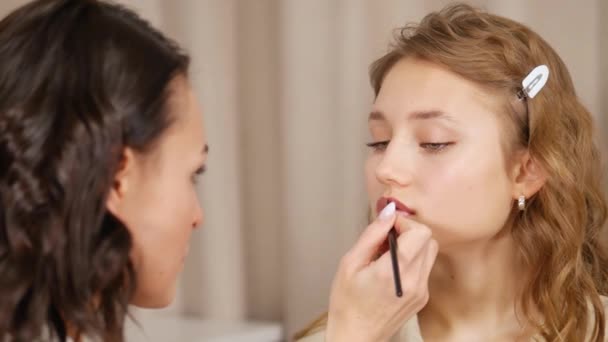 Makeup mästare sätter makeup i ansiktet på klienten. Applicera färg på läpparna på flickan. — Stockvideo