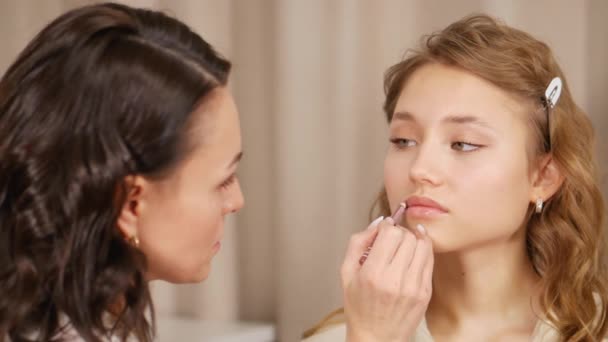 Makeup mästare sätter makeup i ansiktet på klienten. Applicera färg på läpparna på flickan. — Stockvideo