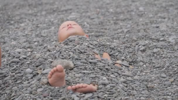 Dítě leží pokryté oblázky. — Stock video