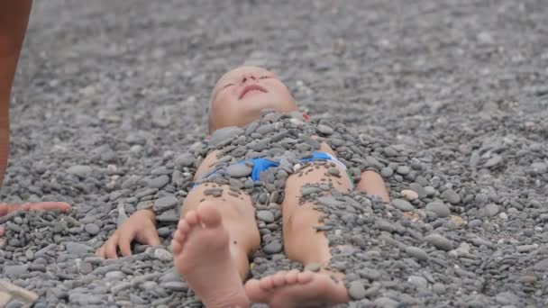 Niño yace cubierto de guijarros . — Vídeos de Stock