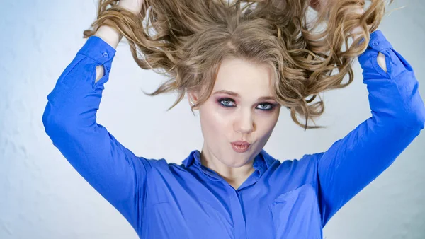 Giovane ragazza bionda solleva ciocche di capelli e li getta. I capelli volano in direzioni diverse. Il viso è nascosto dietro riccioli di capelli. Emozioni chiaramente espresse sul volto delle donne . — Foto Stock