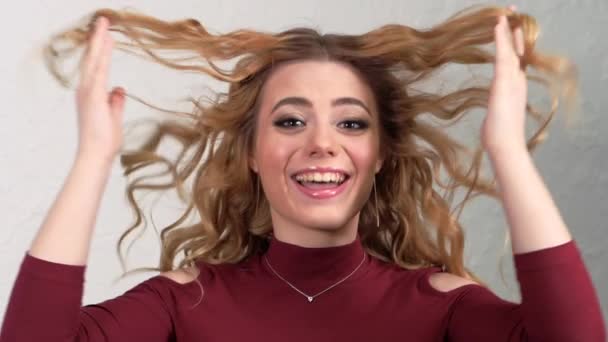 Young blonde girl lifts strands of hair up and throws them. Hair is flying in different directions. The face is hidden behind curls of hair. Clearly expressed emotions on the womans face. — Stok video