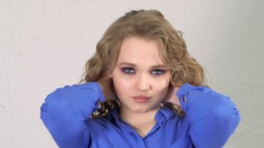 Young blonde girl lifts strands of hair up and throws them. Hair is flying in different directions. The face is hidden behind curls of hair. Clearly expressed emotions on the womans face.