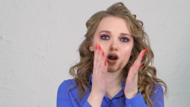 Young blonde girl brings her hands to her face and is very surprised. The face is hidden behind curls of hair. Clearly expressed emotions on the womans face. — Stok video