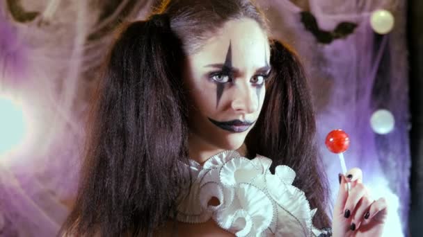 Retrato de una mujer. Un payaso con una sonrisa en corsé con un cuello blanco en el cuello. Modelo con maquillaje para Halloween. Mujer coqueteando. La chica de la piruleta roja . — Vídeos de Stock