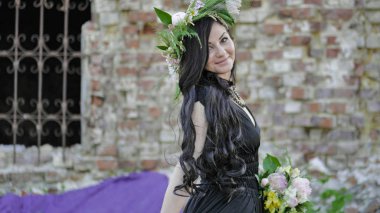 Woman in the spring. A wreath of meadow grass and flowers is worn on the brunettes head. White peonies adorn the head of a young lady. A girl in a long black sleeveless dress.