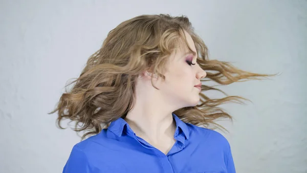 Young blonde girl turns her head. Hair is flying in different directions. The face is hidden behind curls of hair.