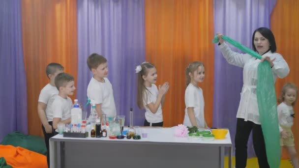 Expériences chimiques pour les enfants. Expériences amusantes pour les enfants. Une femme donne des cours de sciences cognitives. Les enfants mesurent le volume pulmonaire. La fille souffle dans un long sac vert et le gonfle . — Video