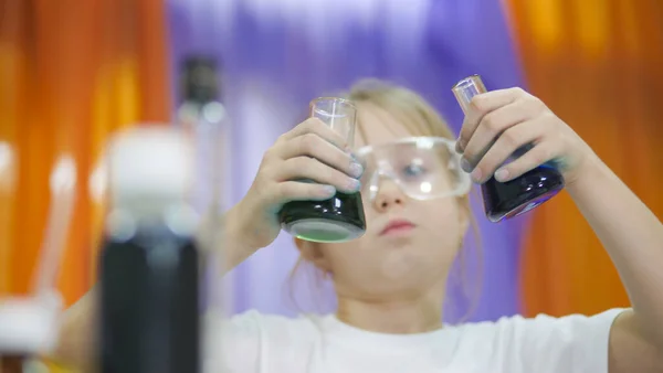 Child is holding flasks of colored liquid. Cute girl in protective transparent glasses on her face. Chemical experiments for children. Fun experiments for children. Children have fun and learn. Bright — Stockfoto