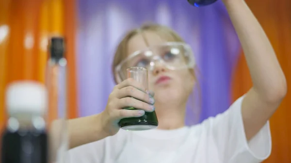 Child is holding flasks of colored liquid. Cute girl in protective transparent glasses on her face. Chemical experiments for children. Fun experiments for children. Children have fun and learn. Bright — ストック写真