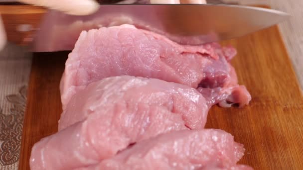 Metallmesser schneidet das Fleisch auf. Fleisch auf einem Holzbrett schneiden. Schweinefleisch steht auf dem Speiseplan. Schweinefleisch in Scheiben geschnitten. Die Hände der Köche waren mit Latexhandschuhen bekleidet. — Stockvideo