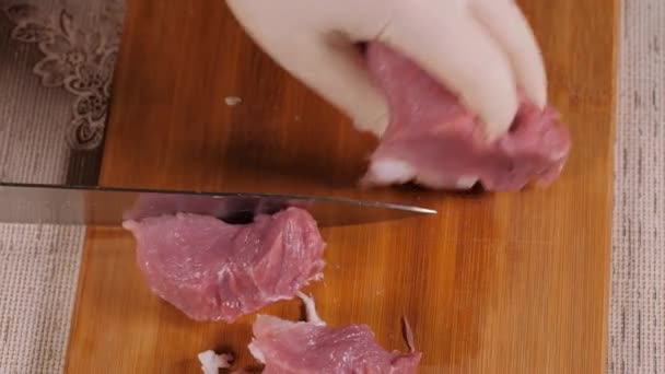 Металлический нож режет мясо. Резал мясо на деревянной доске. Свинина в правлении. Нарезанное мясо свинины. Вид сверху. Руки поваров были одеты в латексные перчатки . — стоковое видео
