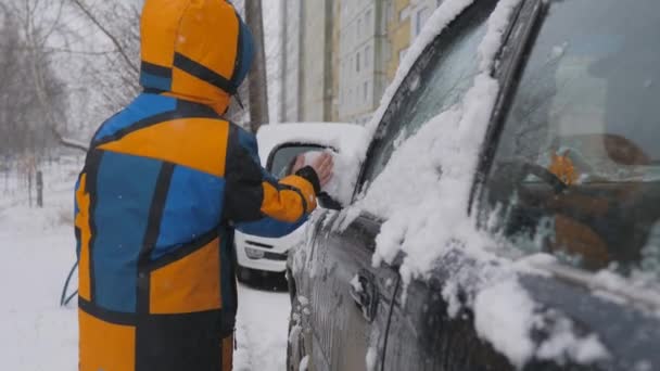 Καθαρισμός του πλευρικού παραθύρου του αυτοκινήτου από το χιόνι. Καθαρισμός του κατόπτρου από το χιόνι από ένα παιδί. Ένα παιδικό χέρι καθαρίζει το γυαλί του αυτοκινήτου. — Αρχείο Βίντεο