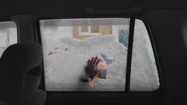 Die Seitenscheibe des Autos vom Schnee befreien. Eine Kinderhand reinigt die Autoscheibe. Der Junge lächelt süß, während er das Glas putzt. — Stockvideo