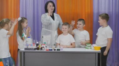 Chemical experiments for children. Boy pours a liquid for a chemical experiment into a plastic Cup with powder. Child tries to pour water on the boys head. Fun experiments for children. Woman pours