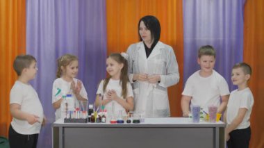 Chemical experiments for children. Fun experiments for children. A woman conducts cognitive science lessons. Children clap their hands in approval as they wait for the class to begin.
