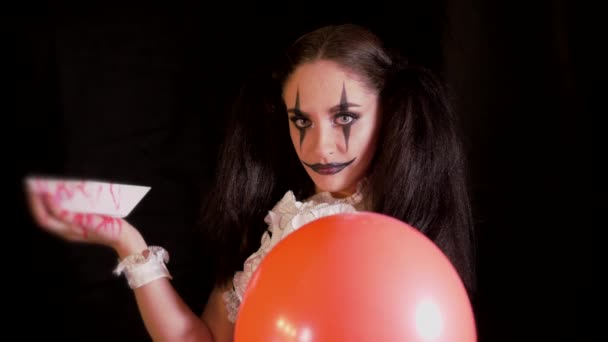 Lätt Halloween makeup. Flicka med en röd ballong i form av en clown. Kvinnan räcker ut handen med den vita båten. På svart bakgrund — Stockvideo
